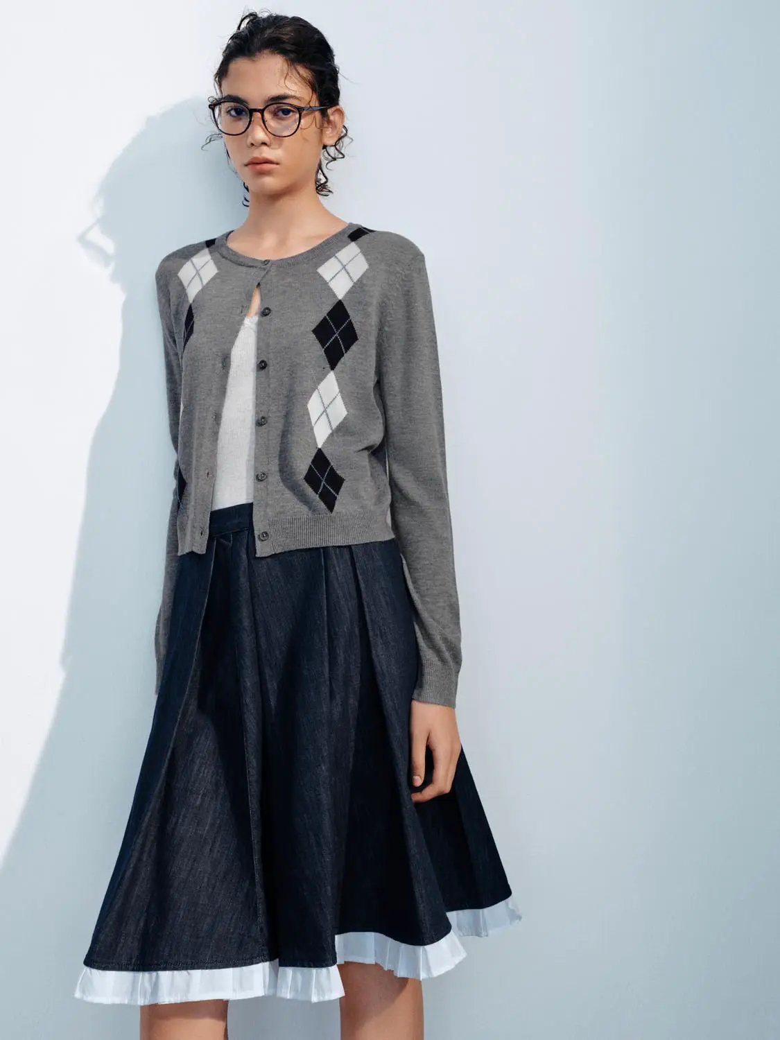 Knit cardigan in grey with white and black argyle pattern; paired with a dark denim skirt