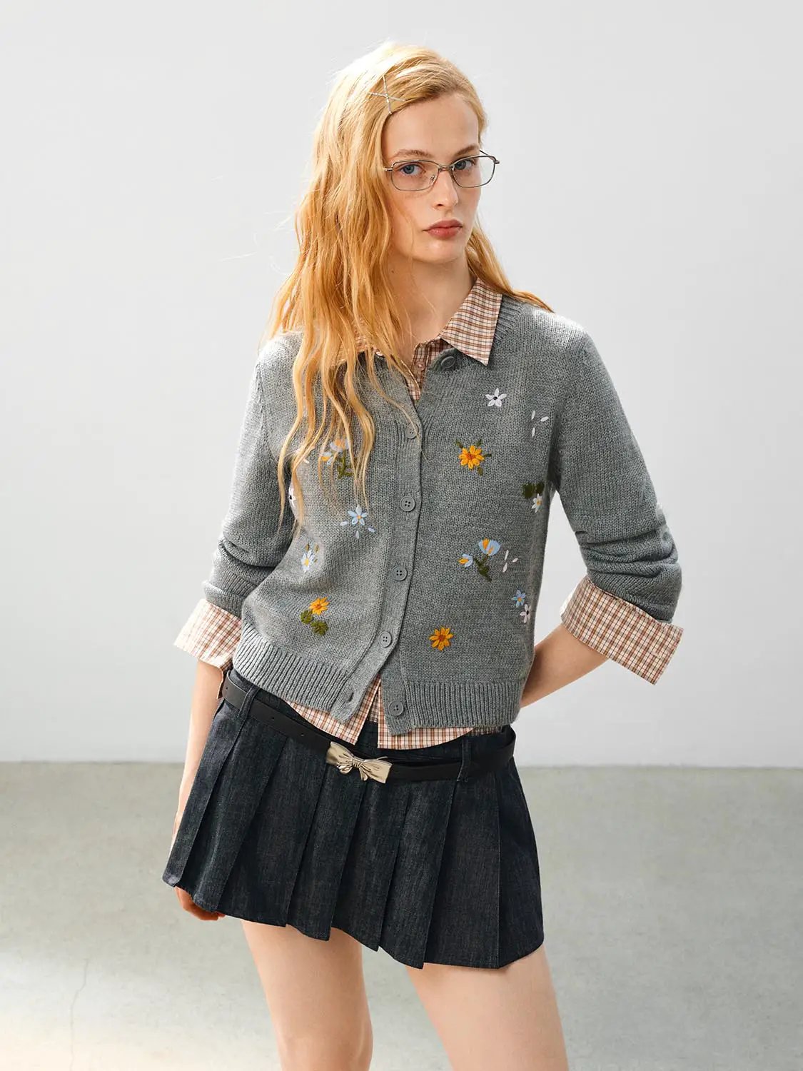Knitted jacket by Urban Revivo in grey with floral embroidery, layered over a plaid shirt.