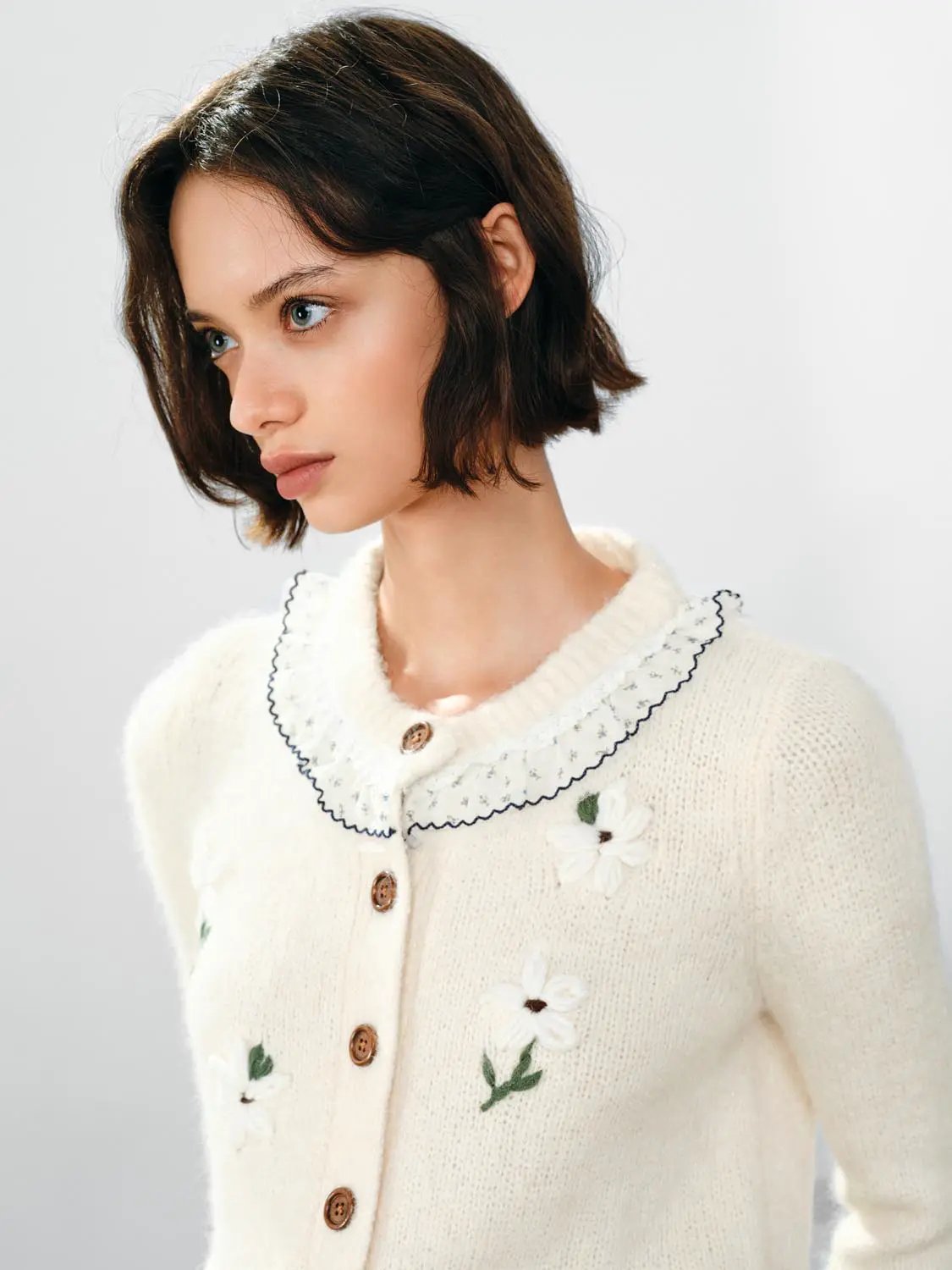 Floral embroidered cream knitted cardigan with navy-trimmed ruffle collar and wooden buttons.