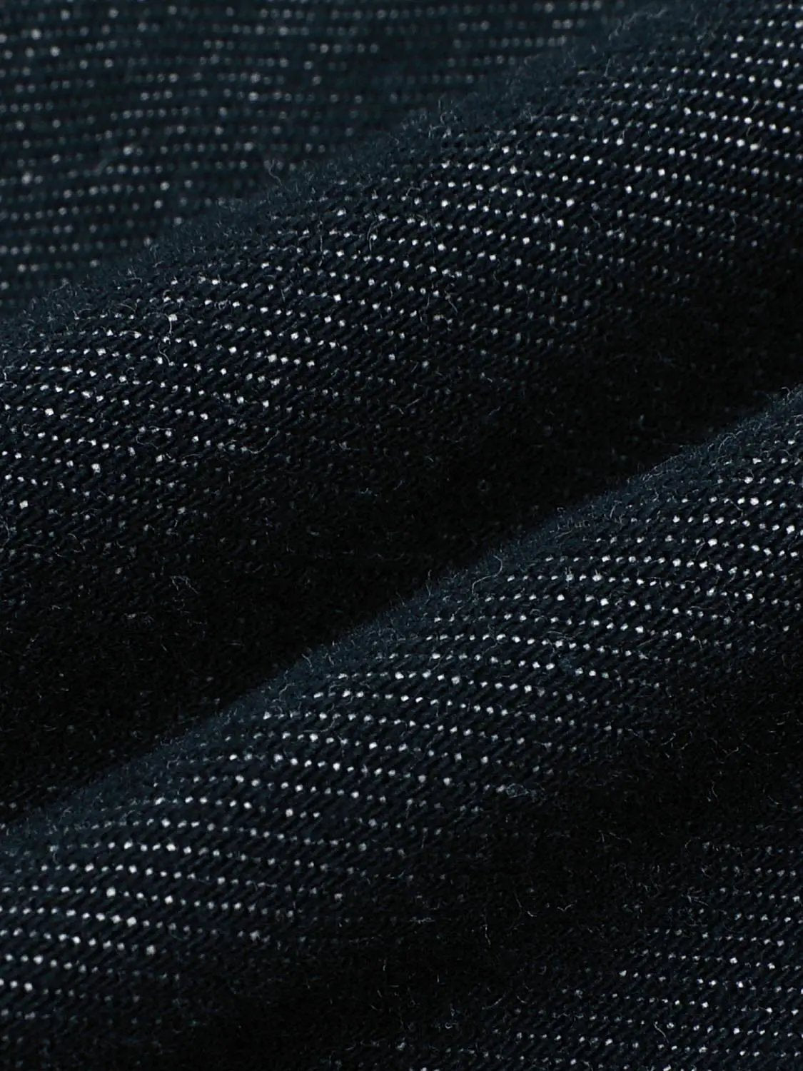 Jeans fabric close-up in dark indigo denim with visible twill texture.