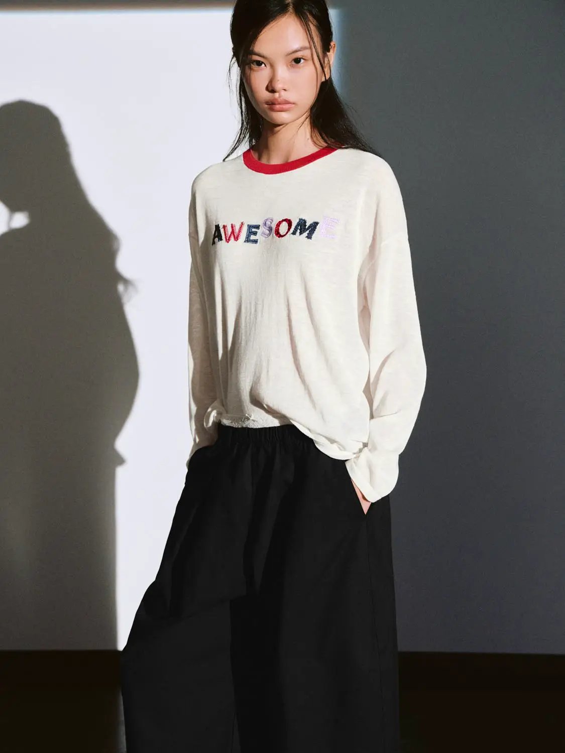 Knitted T-Shirt in off-white with red crew neck and multicolored AWESOME print, paired with black wide-leg pants.