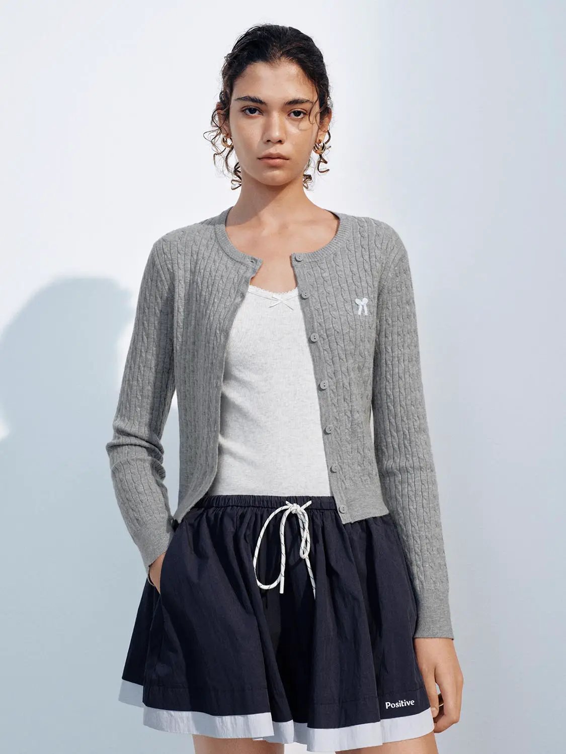 Knit cardigan in grey cable knit with button-front design, worn over a white top.