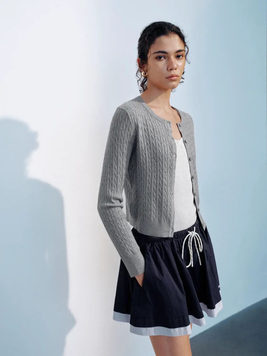 Grey knitted cardigan with cable-knit pattern and button-front, worn over a white tee