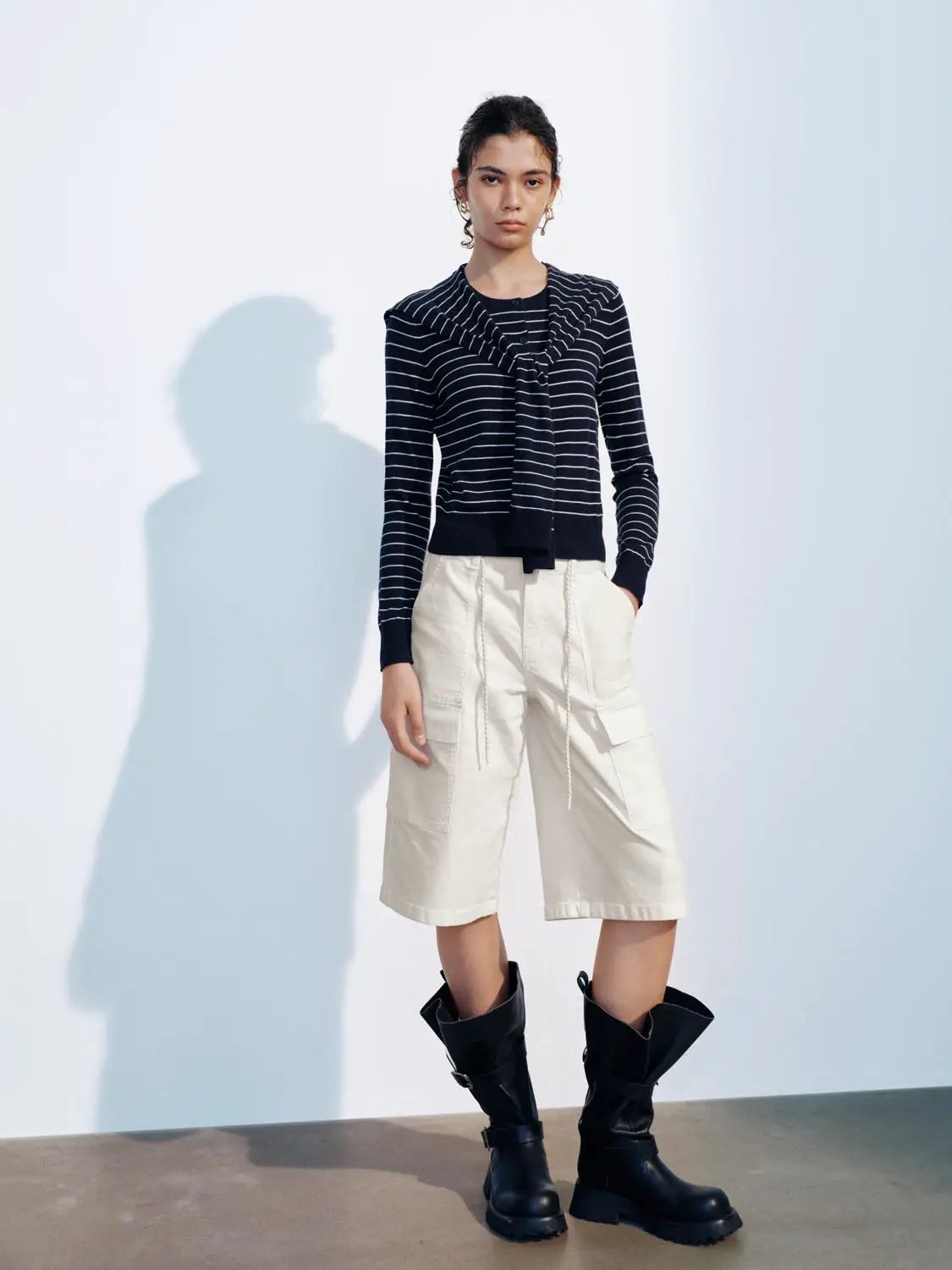 Knitted cardigan navy with white stripes and front tie; worn with beige cargo shorts and black combat boots.