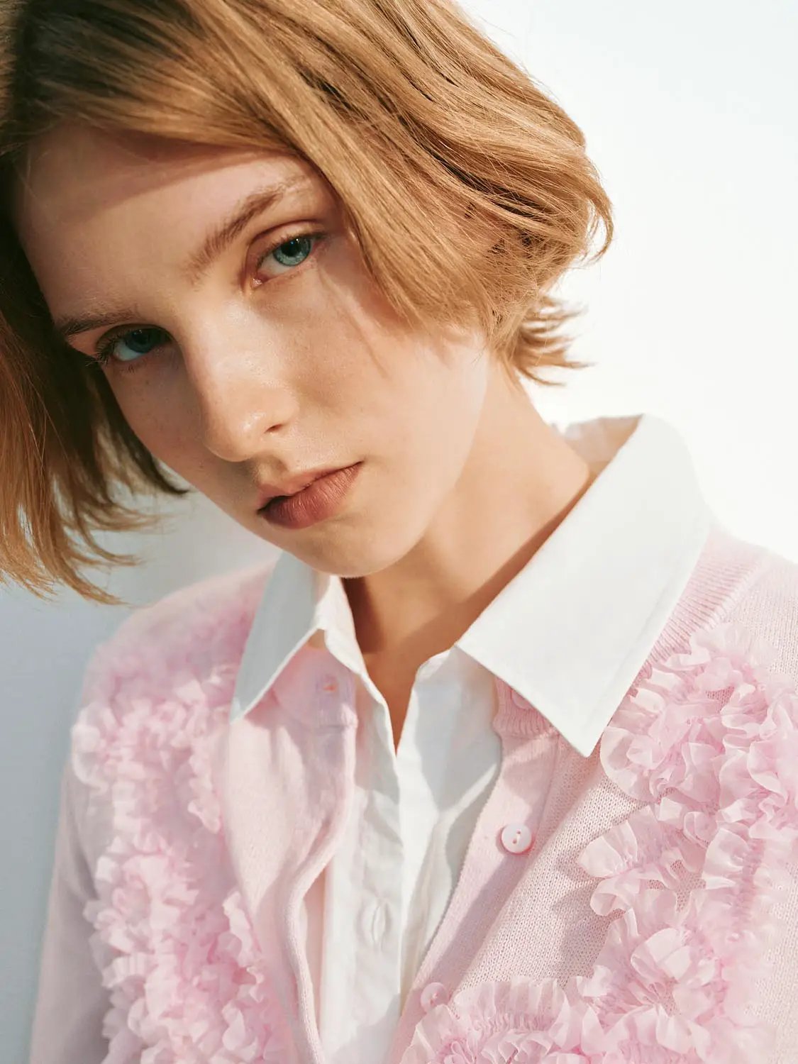 Knitted cardigan in pink with floral appliqués worn over a white shirt