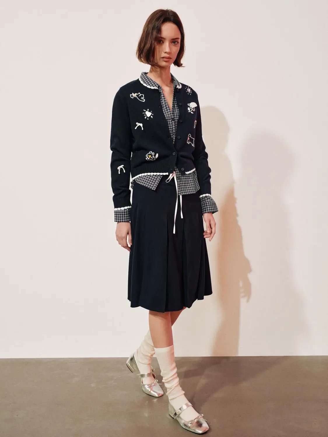 Graphic long sleeve ribbed knit cardigan in navy with white embroidered motifs worn over a checkered shirt