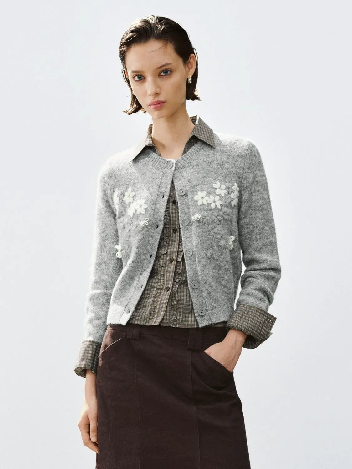 Floral embroidered crew-neck long-sleeve cardigan in light gray, layered over a checked shirt.