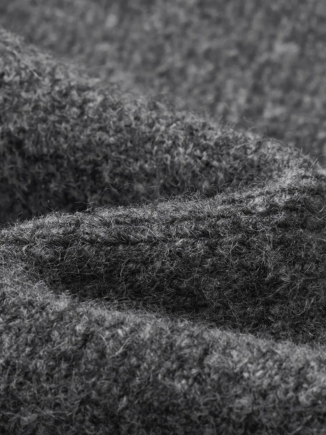 Knitted T-Shirt fabric close-up showing chunky textured gray yarns, subtle fuzz, dense loops, and fibers.