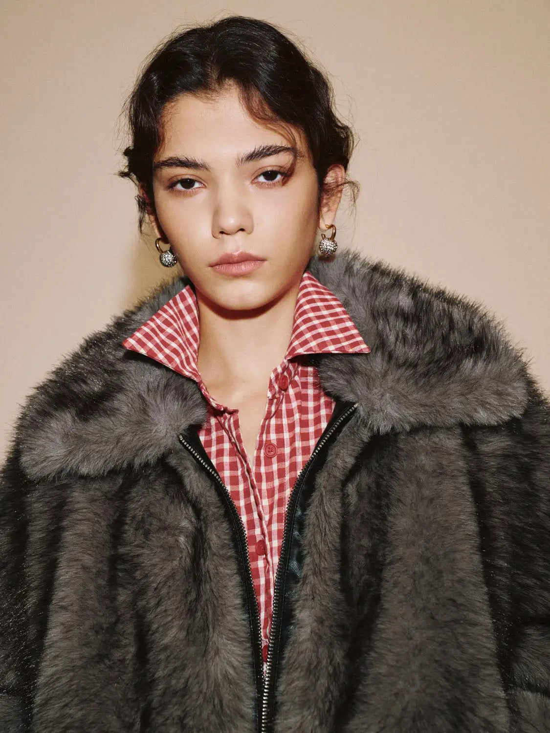 Fur coat in grey with front zipper worn over a red gingham shirt.