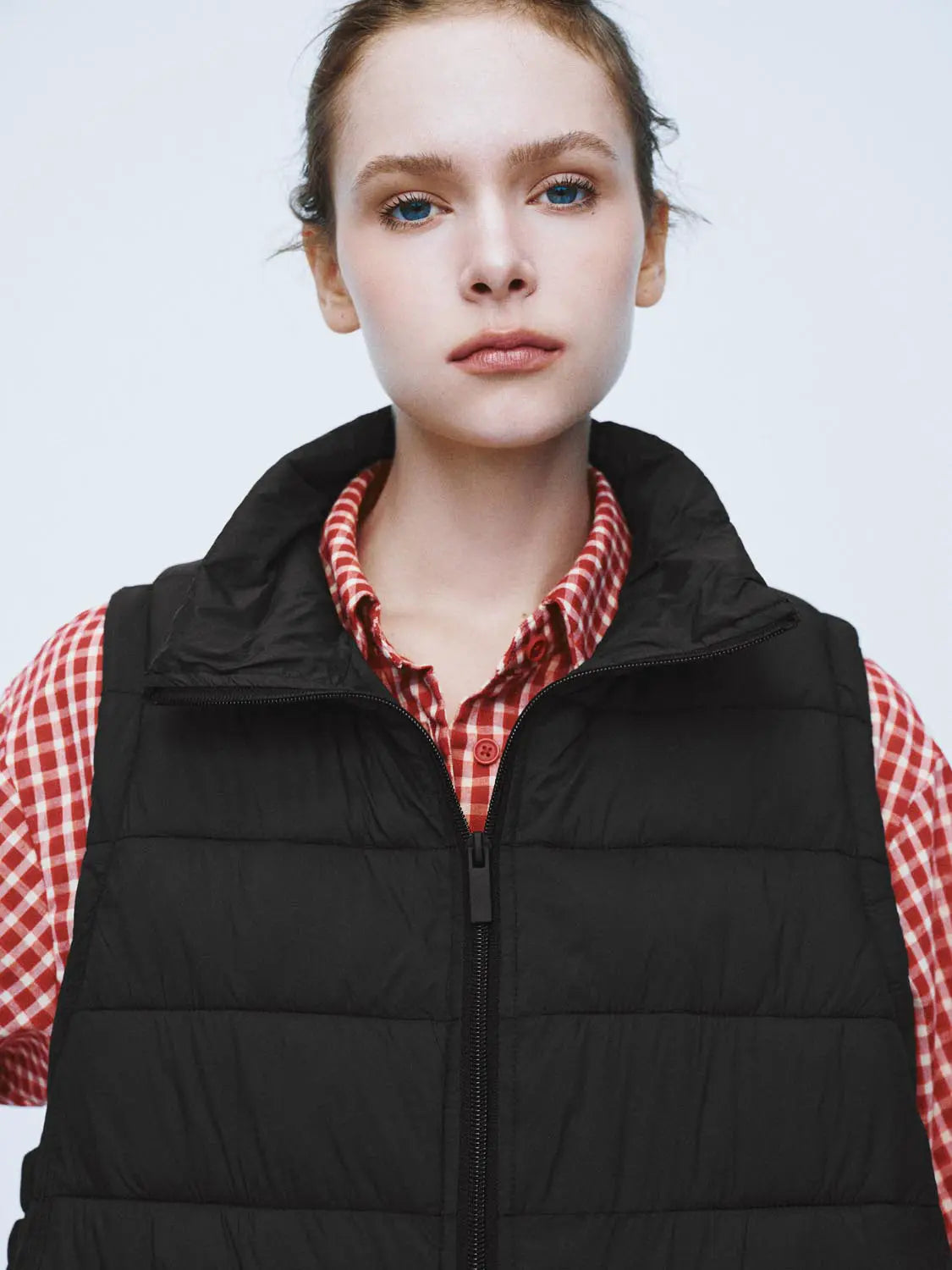 Padded jacket set on model: black quilted vest over red plaid shirt with front zipper