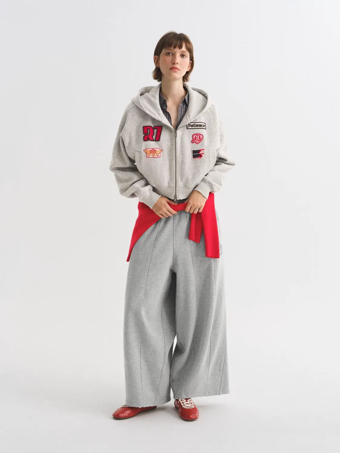 Harem pants in light grey with a wide-leg silhouette; paired with a grey zip hoodie featuring patches
