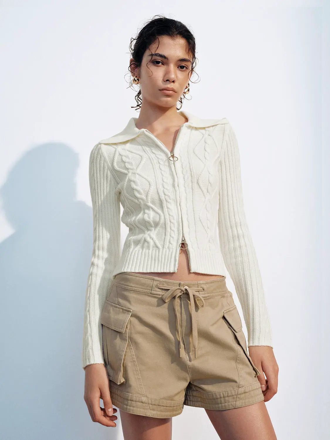 Knit jacket white cable-knit cardigan with zip front and collar, paired with beige cargo shorts.