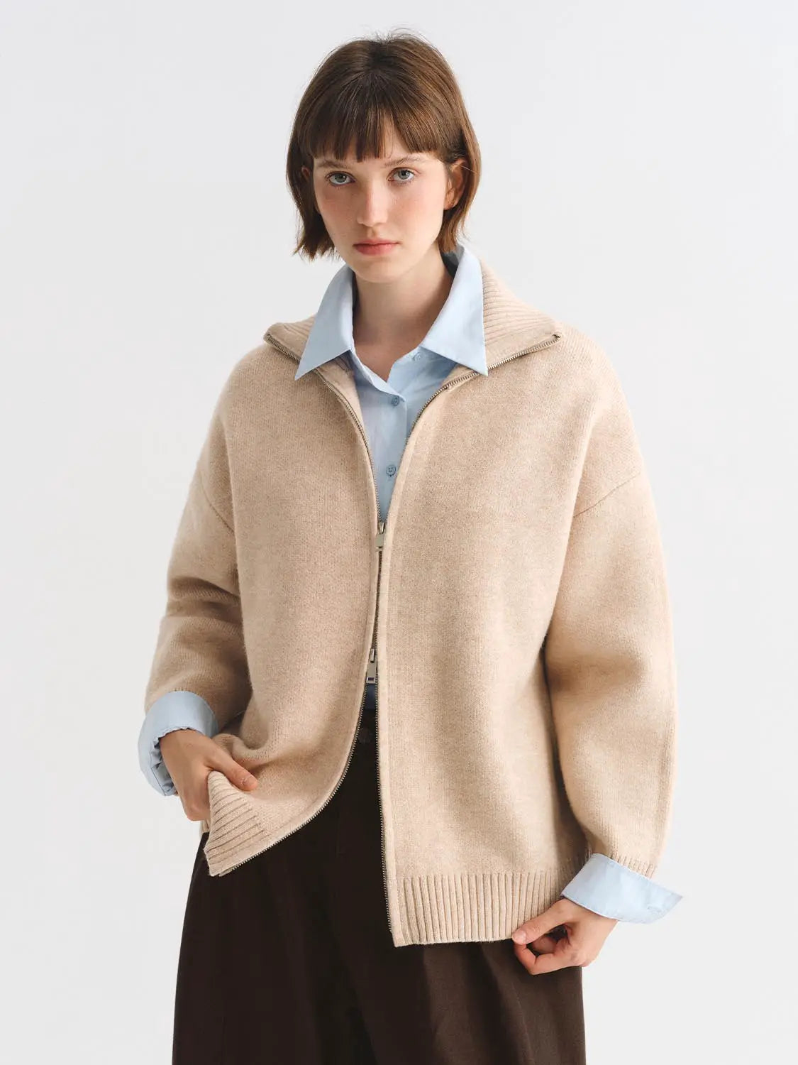 Knit jacket in beige with front zip, worn over a light blue shirt.