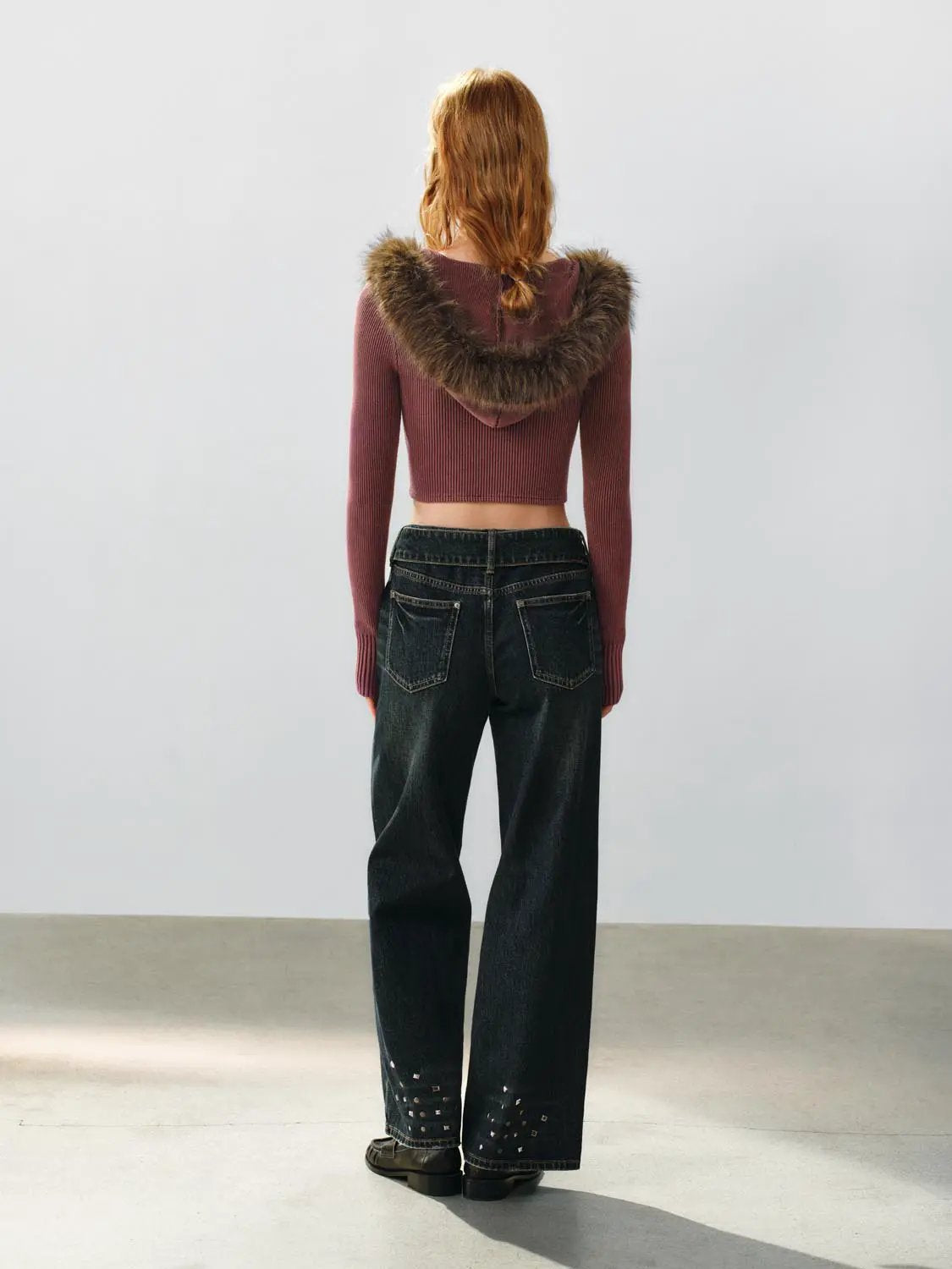 Knit cropped cardigan with a fur-trimmed hood in maroon, back view of a model wearing dark denim jeans