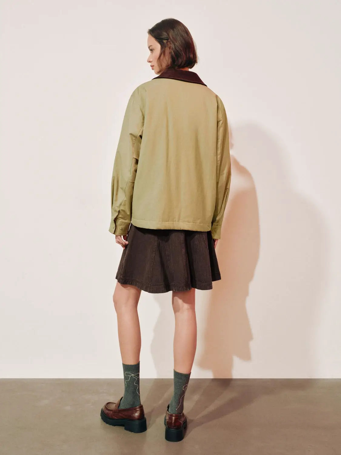 Padded jacket in olive with burgundy collar, back view worn over a dark skirt.