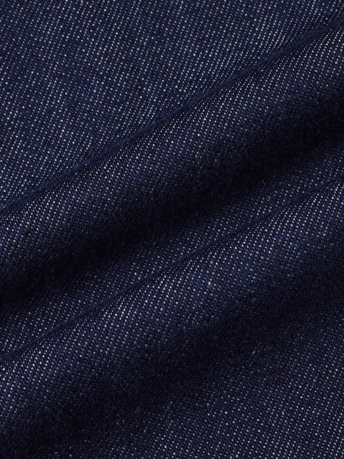 Dark indigo denim pants fabric close-up with visible weave and stitching seam