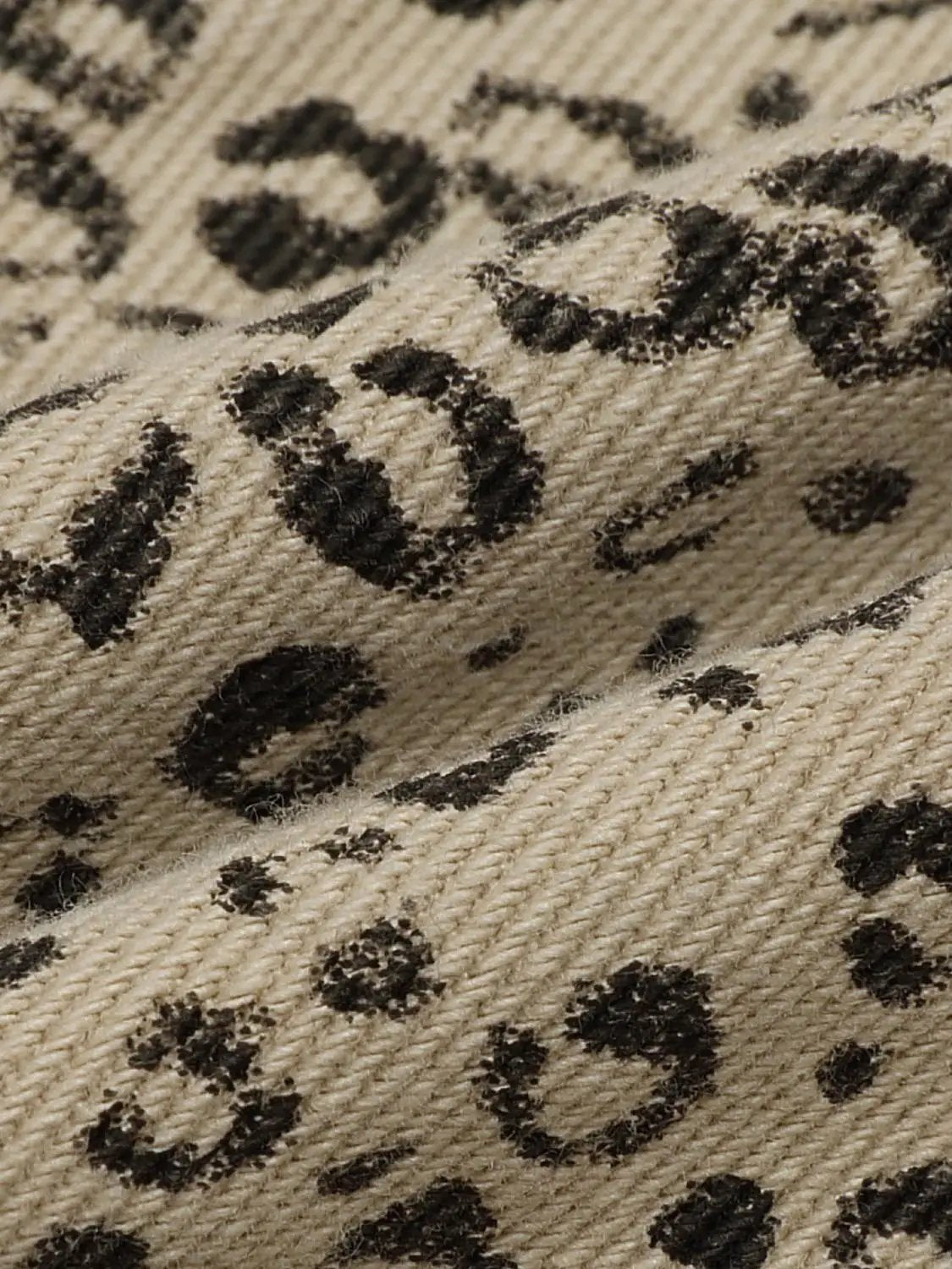 Casual jeans fabric close-up in beige with black printed lettering pattern