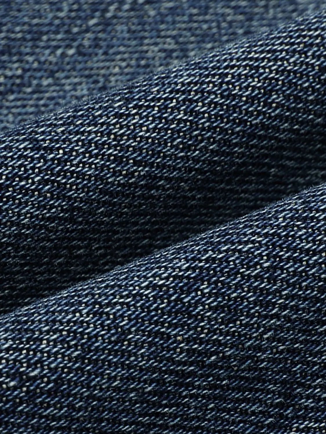 Jeans fabric close-up in dark indigo denim showing textured weave and subtle color variation details