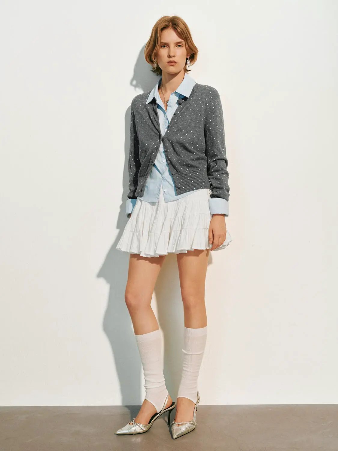 Knitted cardigan in grey with white polka dots, layered over a light blue shirt and a white tiered mini skirt.