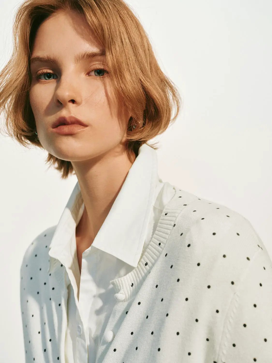 Knitted cardigan with white fabric and black polka dots, worn over a white shirt