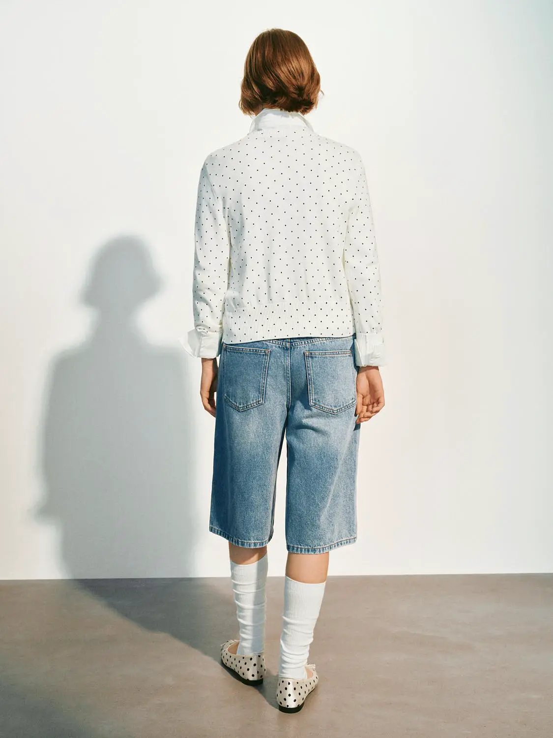 Knitted cardigan in white with black polka dots; long sleeves, back view.