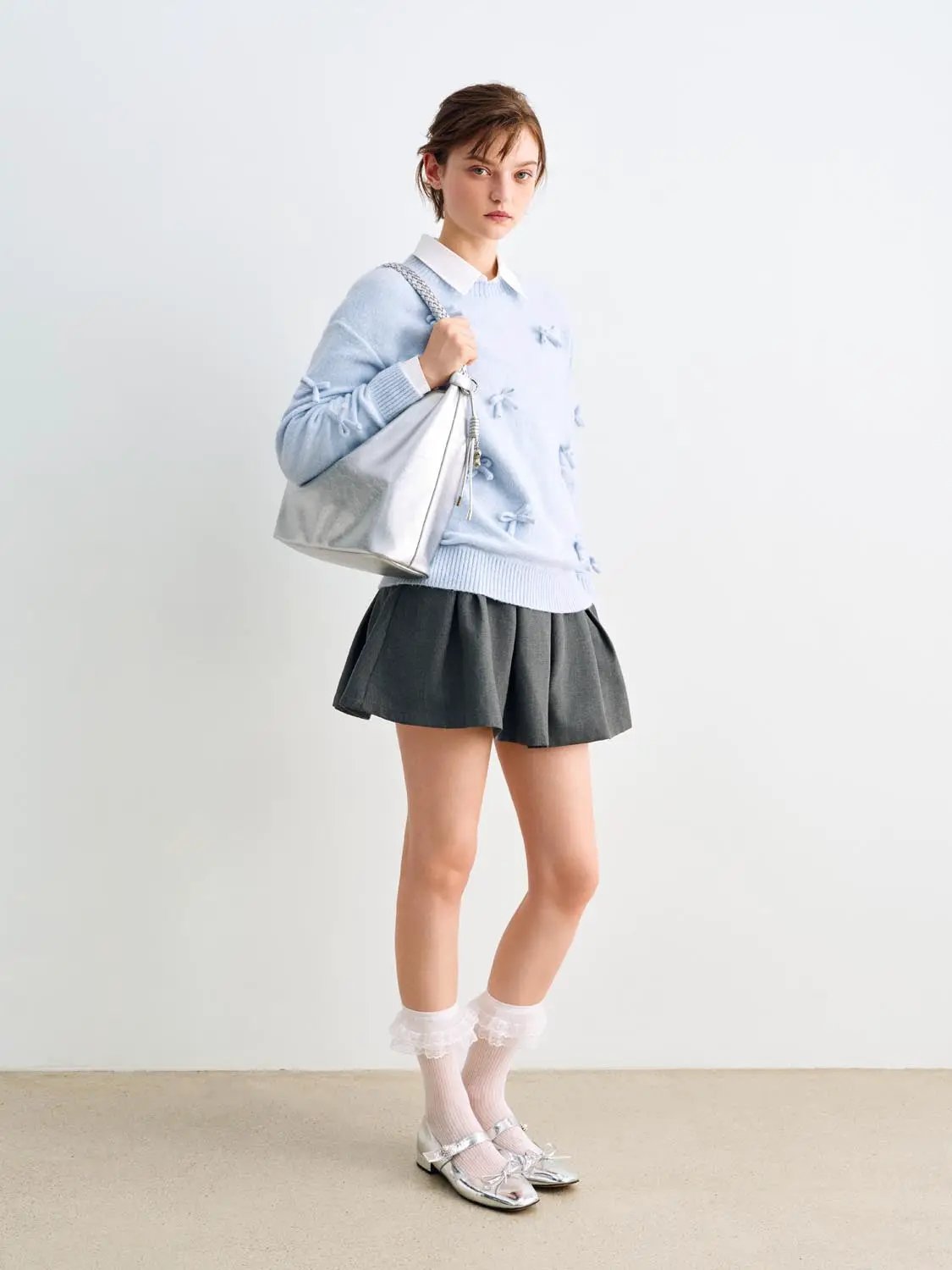 Knit T-Shirt in pale blue with knot detailing; three-piece outfit with gray pleated mini skirt and silver handbag