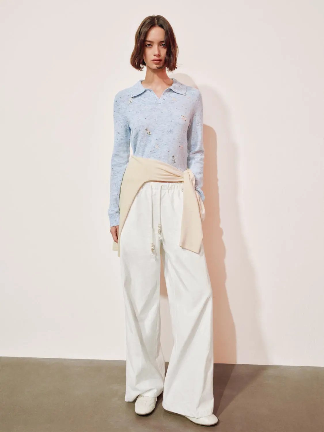 Embroidered floral knit polo-collar sweater, light blue with long sleeves, styled with white wide-leg pants.