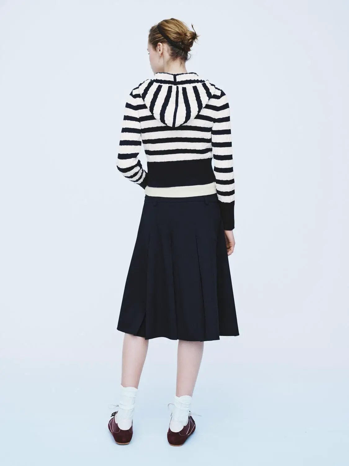 Knitted cardigan with bold black-and-white stripes and hood, paired with a black pleated midi skirt